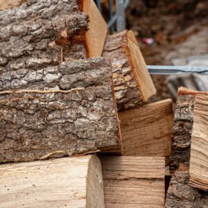 Stack of split firewood pieces with rough bark and a metal tool resting between logs