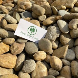 White business card with a green tree logo and 'Pine Straw Place' text resting on tan and gray pebbles.