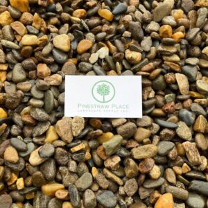 PineStraw Place Landscape Supply Inc. business card with a green tree logo on white paper resting on colorful pebbles.