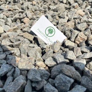White business card with a green tree logo lying among gray rocks/ gravel on the ground.