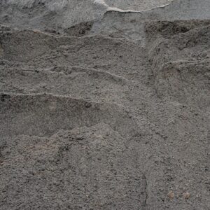 Close-up of dark gray volcanic ash with layered ridges and small pebbles scattered throughout.